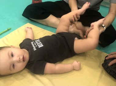 massage for children | AADC News | Rylae-Ann lies on a yellow mat while her mom massages her feet and ankles.